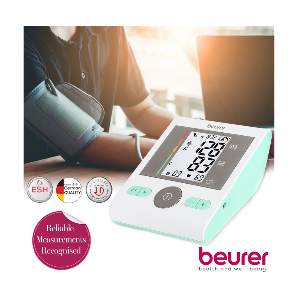User taking a blood pressure measurement at a desk using the clinically validated Beurer BM 29 upper arm monitor with European Society of Hypertension (ESH) recognition badge.